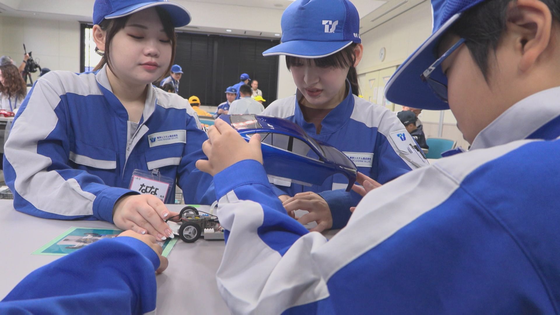 青い作業着のスタッフと子どもが、燃料電池の模型自動車を組み立てている様子
