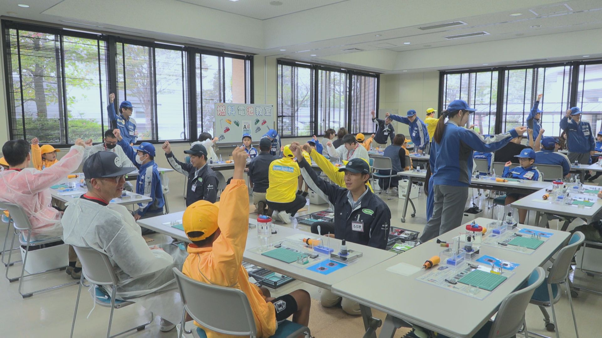 教室いっぱいに集まった子どもたちとスタッフが、拳を上げて笑顔を見せている様子